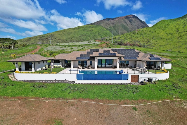 rear view of property featuring a mountain view, a patio area, solar panels, and a yard