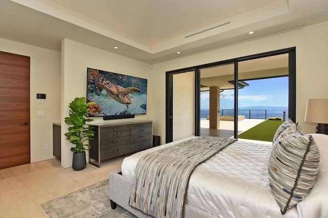 bedroom featuring a raised ceiling, access to exterior, and a water view