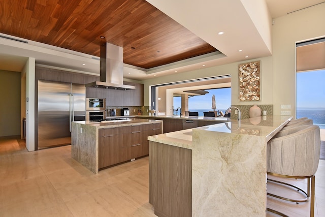 kitchen featuring a water view, a breakfast bar, kitchen peninsula, island range hood, and built in fridge