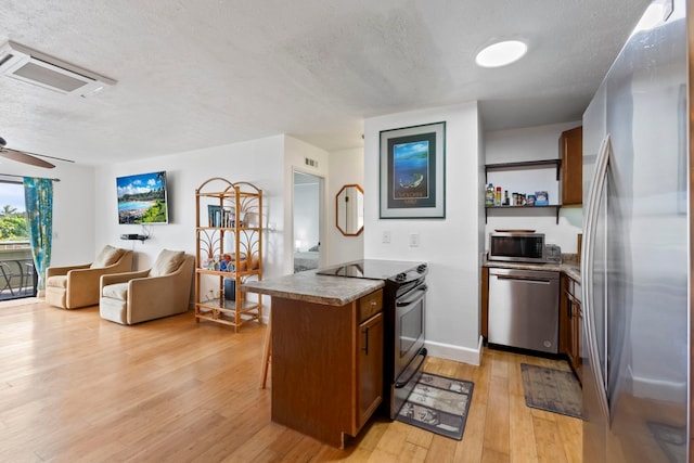 kitchen with ceiling fan, stainless steel appliances, kitchen peninsula, light hardwood / wood-style floors, and a textured ceiling