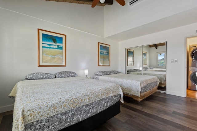 bedroom featuring dark wood-type flooring, stacked washer and dryer, vaulted ceiling with beams, ceiling fan, and a closet