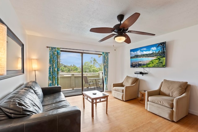 living room featuring ceiling fan, light hardwood / wood-style floors, and a textured ceiling