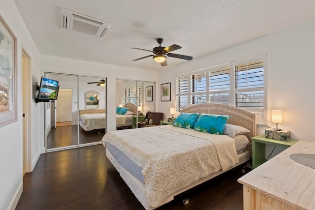 bedroom with dark hardwood / wood-style floors, ceiling fan, and two closets