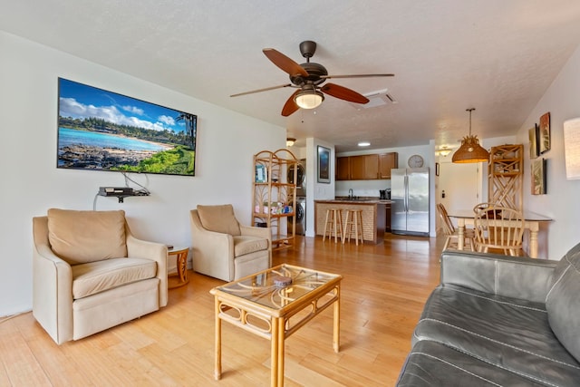 living room with a textured ceiling, light wood-type flooring, and ceiling fan