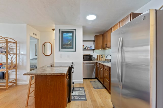 kitchen featuring sink, stainless steel appliances, a kitchen breakfast bar, light hardwood / wood-style floors, and a textured ceiling