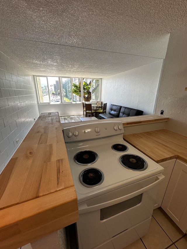 kitchen with backsplash, electric range, white cabinets, light tile patterned floors, and butcher block countertops