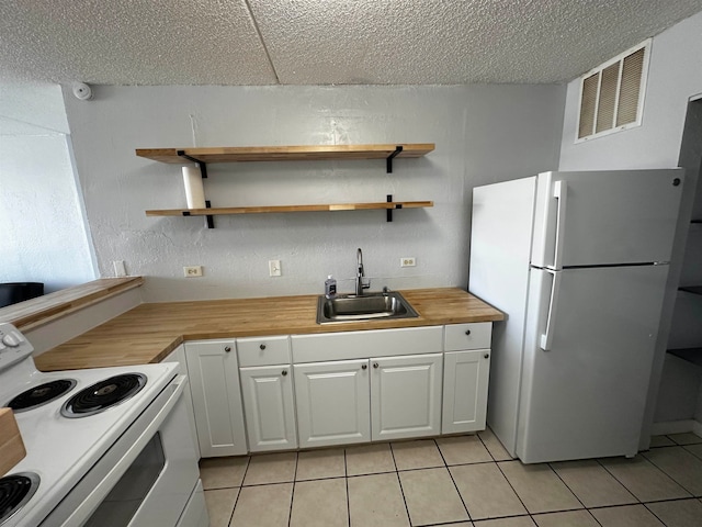 kitchen with white appliances, light tile patterned floors, white cabinetry, sink, and butcher block countertops