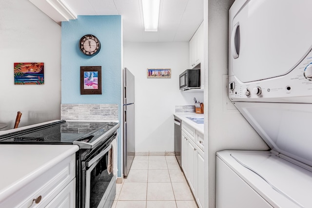 kitchen featuring stainless steel appliances, light tile patterned floors, stacked washing maching and dryer, light countertops, and white cabinets