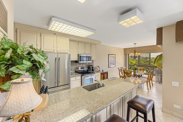 kitchen with sink, light tile patterned floors, stainless steel appliances, light stone countertops, and decorative light fixtures