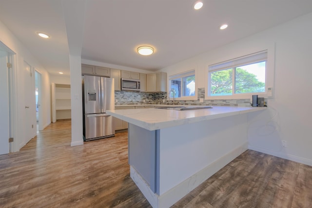 kitchen featuring light stone counters, stainless steel appliances, a peninsula, wood finished floors, and decorative backsplash