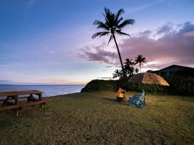 yard at dusk featuring a water view and a fire pit