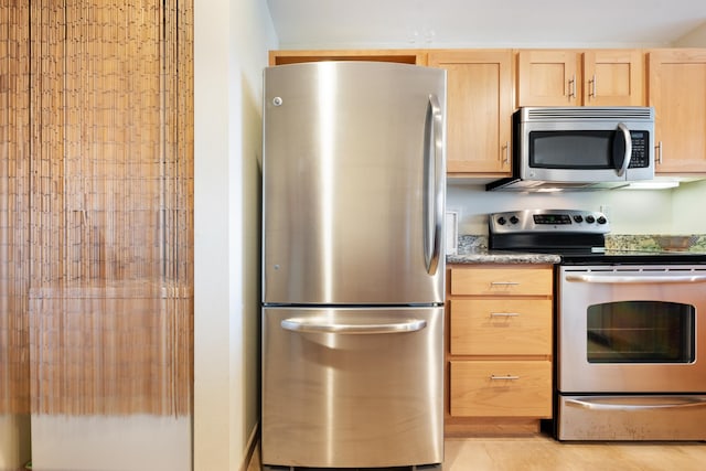 kitchen featuring light brown cabinets, light tile patterned flooring, dark stone counters, and appliances with stainless steel finishes