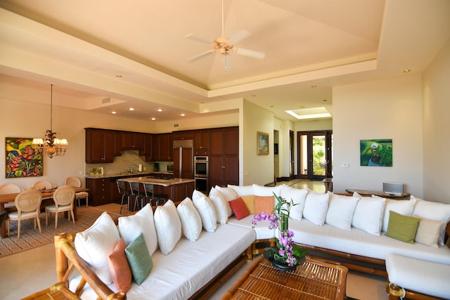 living room featuring a raised ceiling, tile patterned flooring, and ceiling fan with notable chandelier