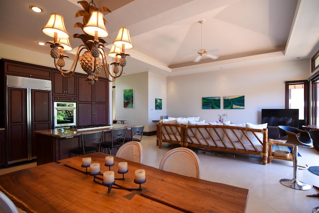 dining area with ceiling fan with notable chandelier, light tile patterned flooring, lofted ceiling, and a tray ceiling