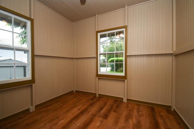 unfurnished room with a healthy amount of sunlight, dark wood-type flooring, and wooden walls