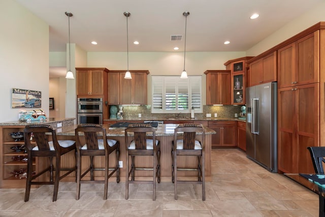 kitchen with appliances with stainless steel finishes, a kitchen breakfast bar, decorative light fixtures, a kitchen island, and light stone counters