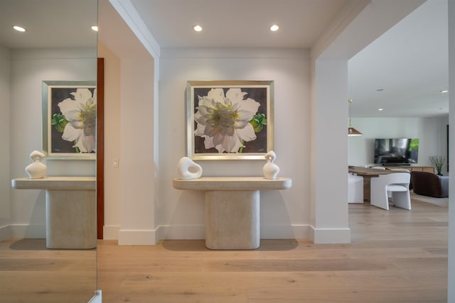 hall with light hardwood / wood-style floors and ornamental molding