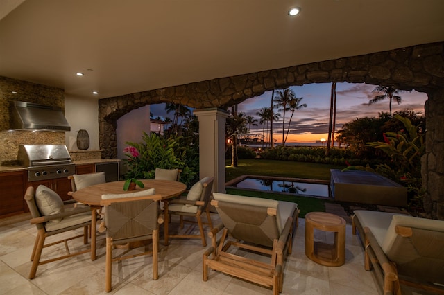 patio terrace at dusk featuring area for grilling and exterior kitchen