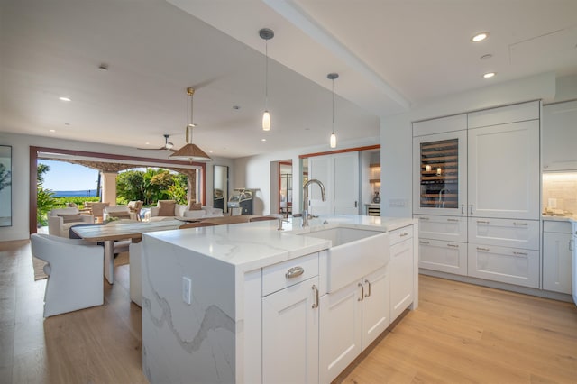 kitchen with a kitchen island with sink, white cabinets, sink, light wood-type flooring, and light stone countertops