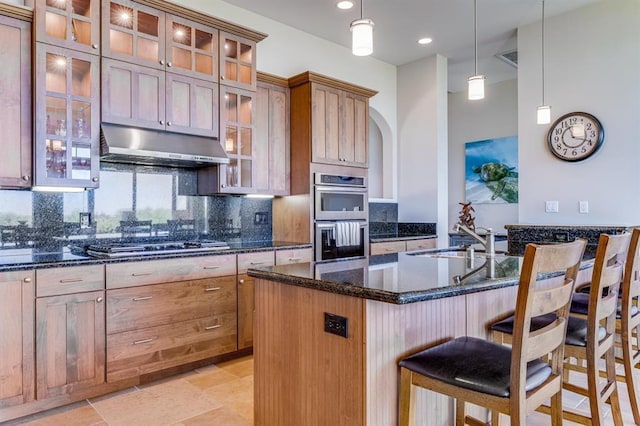 kitchen with appliances with stainless steel finishes, sink, pendant lighting, backsplash, and a center island with sink