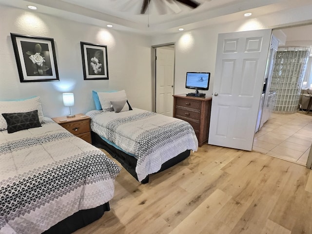 bedroom with light hardwood / wood-style flooring, ceiling fan, and a raised ceiling