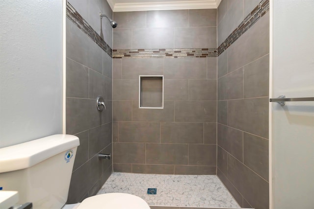 bathroom with ornamental molding, tiled shower, and toilet