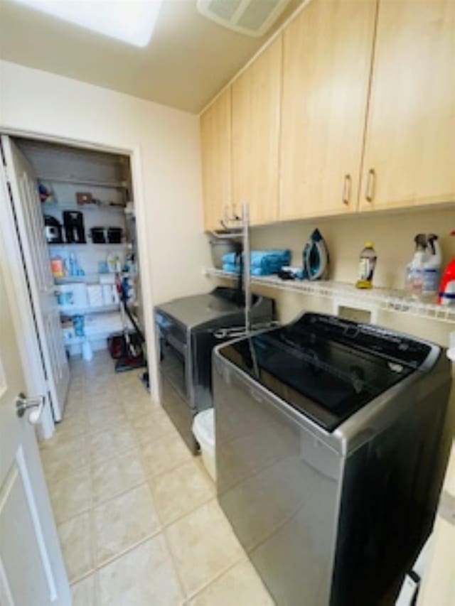 clothes washing area featuring cabinets, light tile patterned floors, and washing machine and clothes dryer