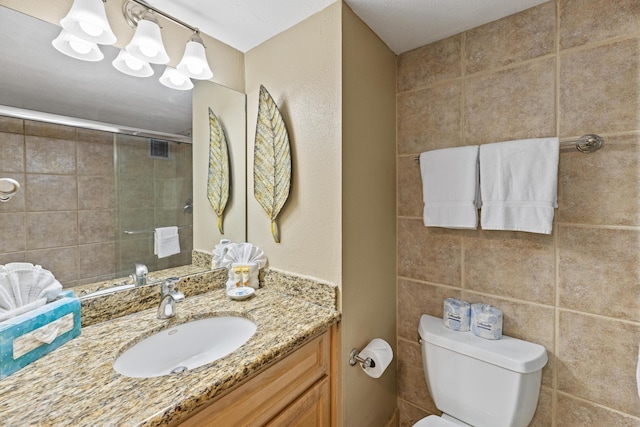 bathroom with vanity, toilet, tile walls, and a shower with shower door