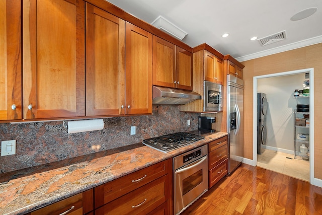 161 Wailea Ike Pl Unit D201, Kihei, HI 96753 - kitchen featuring built in appliances, under cabinet range hood, estacked washer and dryer, brown cabinets, and tasteful backsplash