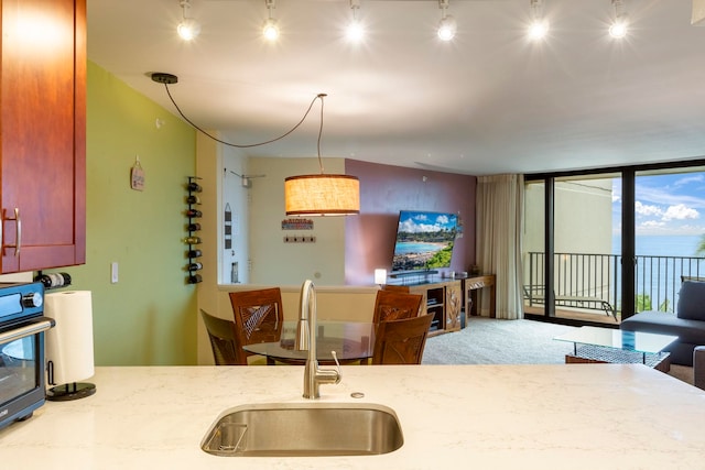 kitchen featuring hanging light fixtures, light stone counters, expansive windows, wall oven, and sink