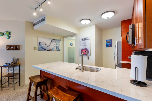 kitchen with kitchen peninsula, a kitchen bar, stainless steel appliances, sink, and light colored carpet