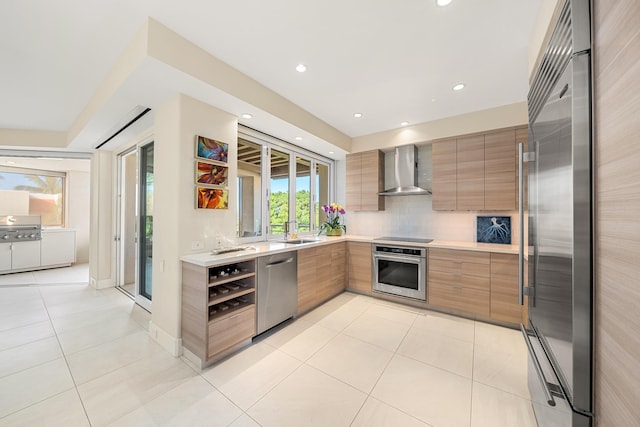 kitchen with wall chimney exhaust hood, sink, light tile patterned floors, stainless steel appliances, and decorative backsplash