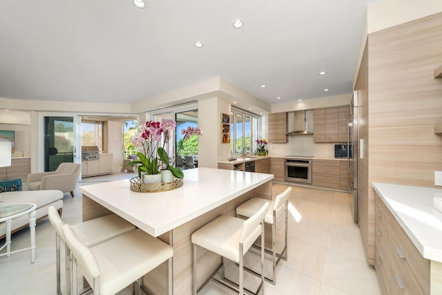 kitchen with wall chimney range hood, a breakfast bar area, oven, and a healthy amount of sunlight