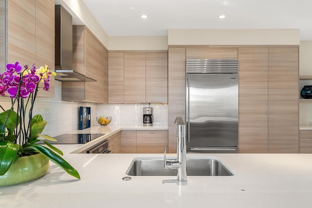 kitchen featuring built in fridge, light brown cabinetry, sink, black electric stovetop, and wall chimney exhaust hood