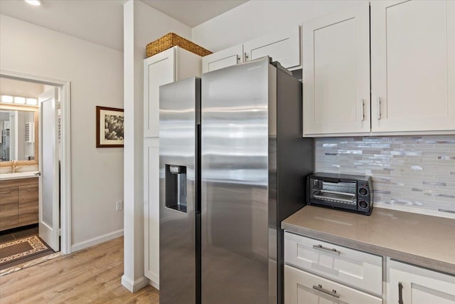 kitchen featuring light hardwood / wood-style floors, white cabinetry, stainless steel refrigerator with ice dispenser, sink, and backsplash