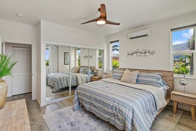 bedroom featuring multiple closets, ceiling fan, a wall mounted AC, and hardwood / wood-style floors