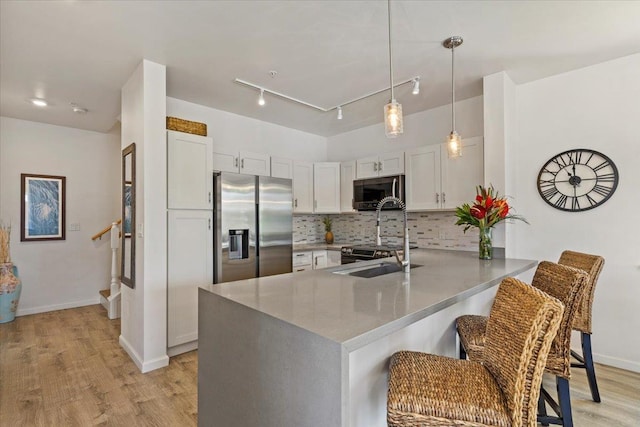 kitchen featuring appliances with stainless steel finishes, white cabinetry, a kitchen breakfast bar, sink, and kitchen peninsula