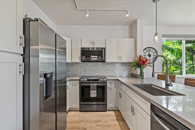 kitchen with appliances with stainless steel finishes, tasteful backsplash, sink, decorative light fixtures, and white cabinets