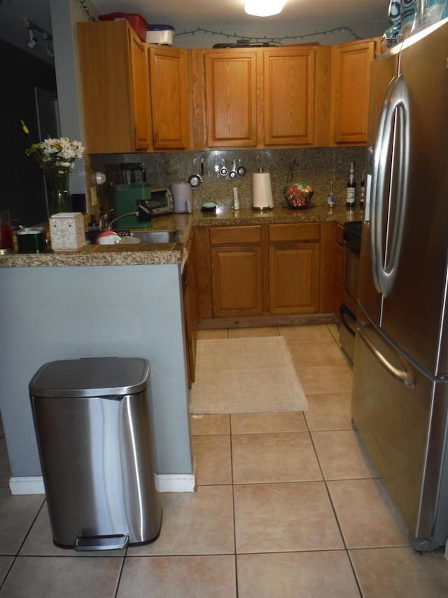 kitchen with light tile patterned floors, brown cabinetry, backsplash, and freestanding refrigerator