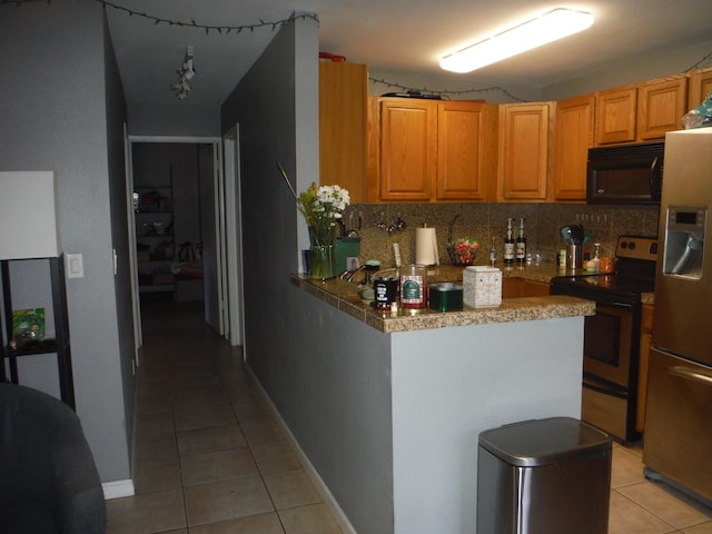 kitchen with black microwave, light tile patterned flooring, refrigerator with ice dispenser, stainless steel range with electric cooktop, and backsplash