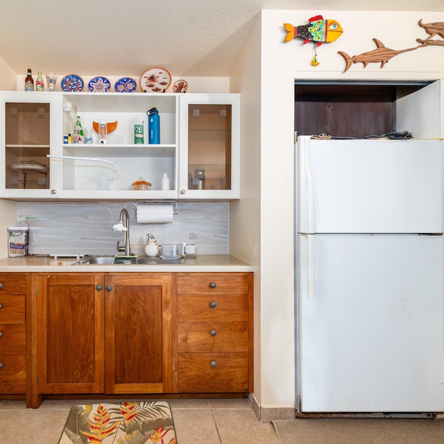 kitchen with white refrigerator, sink, light tile patterned floors, and a textured ceiling