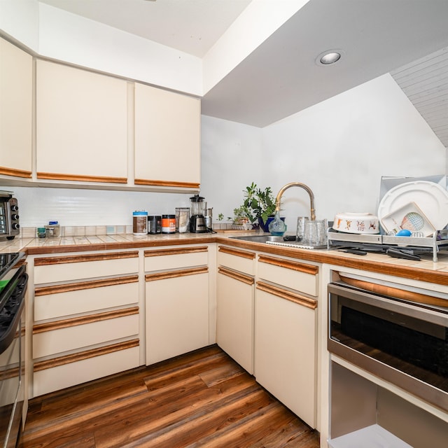 kitchen with appliances with stainless steel finishes, kitchen peninsula, dark hardwood / wood-style flooring, tile countertops, and sink