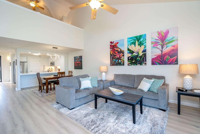 living room with sink, high vaulted ceiling, ceiling fan with notable chandelier, and light wood-type flooring