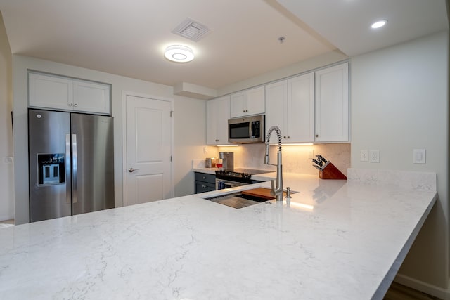 kitchen featuring sink, white cabinetry, light stone counters, appliances with stainless steel finishes, and kitchen peninsula