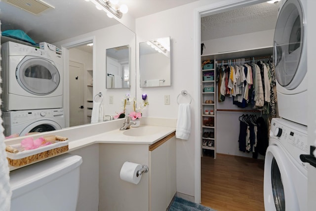 laundry room featuring hardwood / wood-style floors, sink, stacked washer / dryer, and a textured ceiling