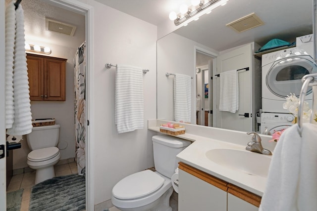 bathroom with tile patterned floors, vanity, stacked washer and dryer, and toilet