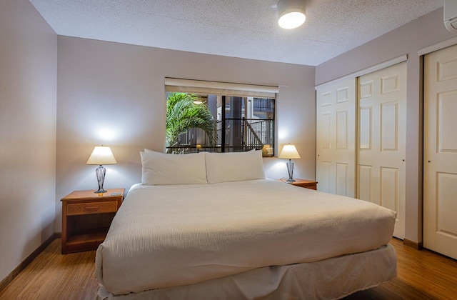 bedroom featuring two closets, a textured ceiling, dark wood-type flooring, and an AC wall unit