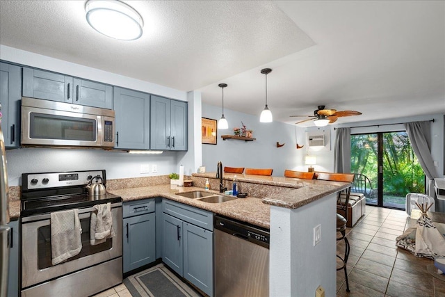 kitchen with a breakfast bar area, light stone counters, appliances with stainless steel finishes, a peninsula, and a sink