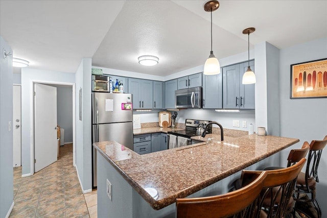 kitchen featuring light stone countertops, a breakfast bar, a peninsula, stainless steel appliances, and decorative light fixtures