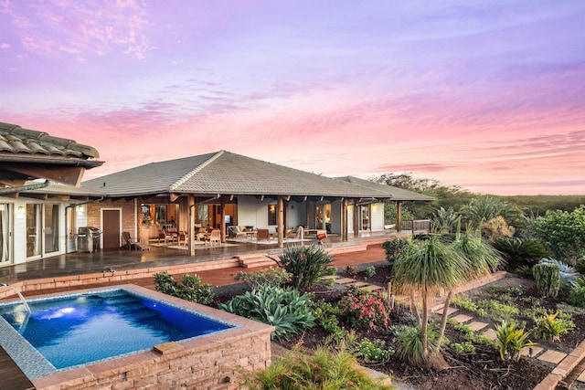 pool at dusk with grilling area and a patio